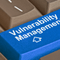 Gros plan sur un clavier d'ordinateur où la touche Entrée, de couleur bleue et marquée du logo d'un média tech, affiche l'inscription en blanc Vulnerability Management pour illustrer la divulgation de failles par un chercheur face à Microsoft.