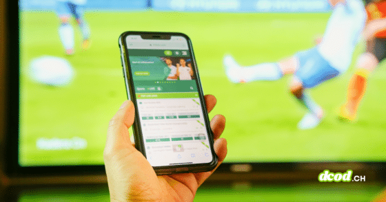 Une main tenant un smartphone affichant une application de paris en ligne devant un match de football, illustrant comment l'illusion de fausses vidéos sur Polymarket dupe les internautes.