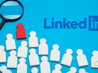 Illustration conceptuelle sur fond bleu montrant le logo LinkedIn, une loupe et une figurine rouge isolée au milieu de nombreuses figurines blanches, évoquant l'alerte du FBI et du MI5 sur les faux recrutements sur LinkedIn.