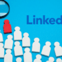Illustration conceptuelle sur fond bleu montrant le logo LinkedIn, une loupe et une figurine rouge isolée au milieu de nombreuses figurines blanches, évoquant l'alerte du FBI et du MI5 sur les faux recrutements sur LinkedIn.