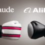 Une photographie de studio nette montrant deux mains portant des gants de boxe s'affrontant sur un fond gris neutre. La main gauche porte un gant de boxe blanc avec trois bandes fuchsia fuchsia, associée au logo étoile orange et au texte 'Claude' superposé. La main droite porte un gant de boxe noir uni, associée au logo vagues stylisées et au texte 'Alibaba' superposé. Les deux paires se font face dans un geste d'affrontement ou de combat symbolique. Le filigrane 'dcod.ch' est en bas à droite. Les logos et textes sont clairs.
