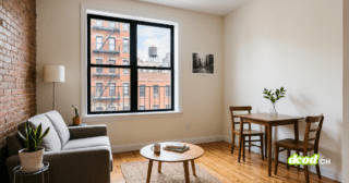 Photographie de l'intérieur d'un appartement typique à New York, avec un canapé gris et un coin repas. La grande fenêtre montre des façades d'immeubles avec escaliers de secours et un château d'eau. Cette image illustre un type de logement numérique faisant l'objet d'annonces immobilières susceptibles d'être retouchées par l'IA immobilier.