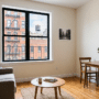 Photographie de l'intérieur d'un appartement typique à New York, avec un canapé gris et un coin repas. La grande fenêtre montre des façades d'immeubles avec escaliers de secours et un château d'eau. Cette image illustre un type de logement numérique faisant l'objet d'annonces immobilières susceptibles d'être retouchées par l'IA immobilier.