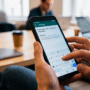 Photographie à la première personne montrant un homme en gros plan saisissant un nom d'utilisateur sur l'application WhatsApp de son smartphone Android, avec l'écran affichant "Créer votre nom d'utilisateur WhatsApp" et "@user_". Le logo DCOD.CH est visible dans le coin inférieur droit.