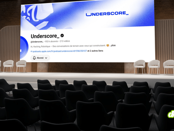 Une salle de conférence vide avec des sièges noirs au premier plan et une scène avec quatre chaises blanches à l'arrière-plan. Sur le grand écran de scène, on voit la page d'accueil YouTube de la chaîne 'Underscore_'