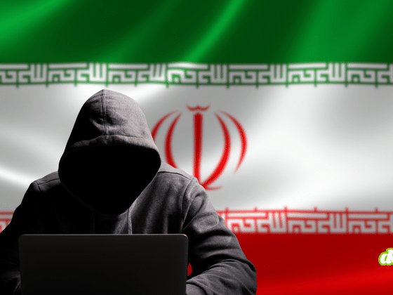 Silhouette sombre d'un pirate informatique en sweat à capuche devant un ordinateur portable, posant devant le drapeau national iranien.