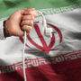 Texte alternatif (alt) : Une main débranche une prise électrique sur fond du drapeau de l'Iran, illustrant la cyberattaque contre une centrale électrique au Royaume-Uni.