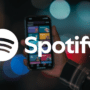 Logo Spotify et main tenant un smartphone affichant l'application, illustrant la décision de Spotify d'exclure les faux artistes IA de ses recommandations.