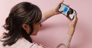 Une femme tient un smartphone affichant un visage analysé par un maillage numérique bleu, illustrant l'authentification et l'analyse visuelle par IA.