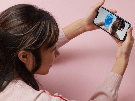 Une femme tient un smartphone affichant un visage analysé par un maillage numérique bleu, illustrant l'authentification et l'analyse visuelle par IA.