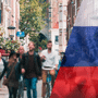Rue commerçante européenne avec des passants, superposée au drapeau russe, illustrant les opérations en zone grise en Europe.