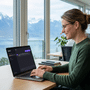 Une professionnelle utilise l’assistant IA Lumo avec le modèle suisse Apertus 1.5 sur son ordinateur portable dans un bureau avec vue sur un lac et les Alpes.