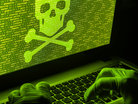Mains gantées sur un ordinateur portable affichant du code vert et une tête de mort, illustrant la cyberattaque de ShinyHunters contre le groupe Clop.