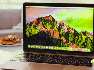 Ordinateur portable Apple MacBook ouvert affichant le bureau de macOS sur une table, illustrant le système d'exploitation et ses paramètres de sécurité Full Disk Access.