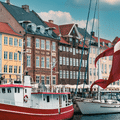 Drapeau danois flottant devant les façades colorées et les bateaux amarrés sur un canal de Copenhague.