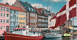 Drapeau danois flottant devant les façades colorées et les bateaux amarrés sur un canal de Copenhague.