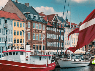 Drapeau danois flottant devant les façades colorées et les bateaux amarrés sur un canal de Copenhague.