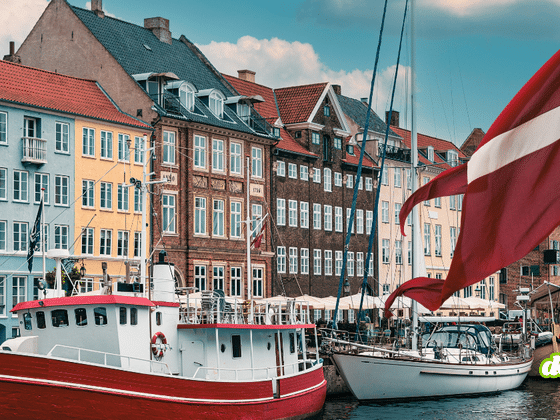 Drapeau danois flottant devant les façades colorées et les bateaux amarrés sur un canal de Copenhague.