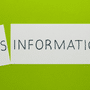 Sur un fond vert vif, une feuille de papier blanche a été coupée en deux, séparant le mot « DISINFORMATION » écrit en lettres capitales noires. Le petit morceau de gauche, légèrement incliné, porte l'inscription « DIS », tandis que le grand morceau de droite affiche « INFORMATION ».