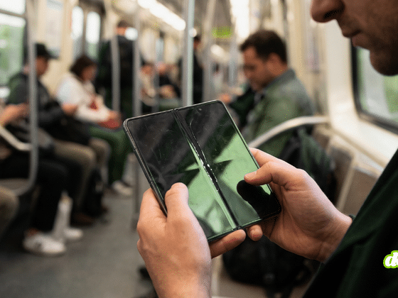 Gros plan sur un smartphone pliable tenu en main, montrant une fissure prononcée et un pli marqué au centre de l'écran intérieur éteint.