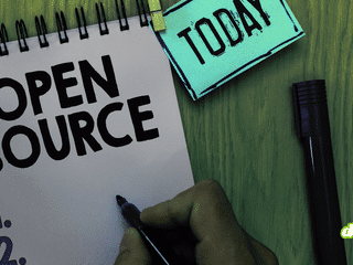Main tenant un feutre noir au-dessus d'un carnet à spirales où est inscrit Open Source, illustrant le programme de sécurité de Google.