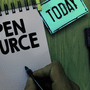 Main tenant un feutre noir au-dessus d'un carnet à spirales où est inscrit Open Source, illustrant le programme de sécurité de Google.