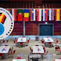 Vue générale de la grande salle de compétition de l'European Cybersecurity Challenge 2026 à Bochum avec les tables des délégations, surmontée des drapeaux des pays participants et du logo officiel de l'événement. — © Bochum Wirtschaftsentwicklung | Donna & der Blitz
