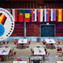 Vue générale de la grande salle de compétition de l'European Cybersecurity Challenge 2026 à Bochum avec les tables des délégations, surmontée des drapeaux des pays participants et du logo officiel de l'événement. — © Bochum Wirtschaftsentwicklung | Donna & der Blitz