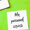 Note adhésive blanche posée à côté d'un clavier d'ordinateur portable sur fond vert, portant l'inscription manuscrite « My password 123456 ».