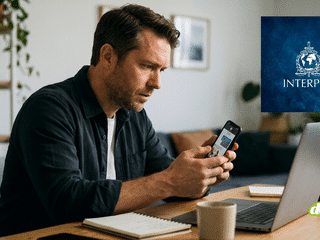 Professionnel observant avec méfiance un message reçu sur son smartphone devant son ordinateur portable.