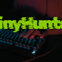Mains d'un informaticien tapant sur un clavier rétroéclairé dans la pénombre, avec le nom du groupe cybercriminel ShinyHunters inscrit en lettres vertes stylisées.