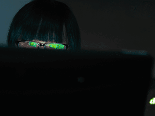 Pirate informatique observant un écran dans l'obscurité avec des reflets verts sur ses verres de lunettes, illustrant le vol de données du FBI par ShinyHunters.